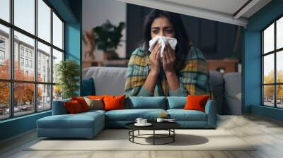 Unhappy sad young indian female in plaid suffering from fever and flu on sofa, blowing nose in napkin in living room interior. Covid-19 lockdown, treatment of illness, cold and runny,  : Generative AI Wall mural