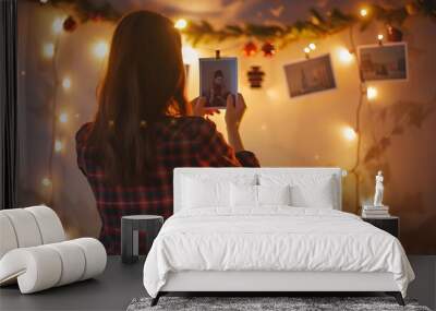 Young beautiful woman hangs a photos on a garland with light on the wall Bokeh girl in red checkered shirt comfort at home New Years mood Christmas decorations : Generative AI Wall mural