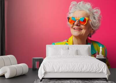 Happy Senior Retired Woman in Colorful Clothing and Sunglasses Against a Pink Background Wall mural