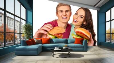 Couple eating fast food. Man and woman eat hamburger with ham. Friends holding two burder junk on white background isolated. Loving couple prefers fast food to homemade dinner. Discounts for fast food Wall mural