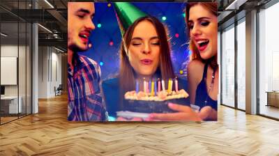 Happy friends birthday party with candle celebration cakes. People looking at burning candles. Two women and men have fun in nightclub. Wall mural