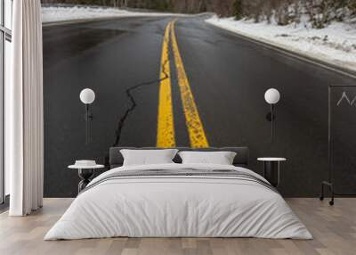 Wintertime Road Landscape With Two Parallel Yellow Solid Lines And A Long Crack Due To Cold Weather With Snow Covered Pine Trees In The Background Wall mural