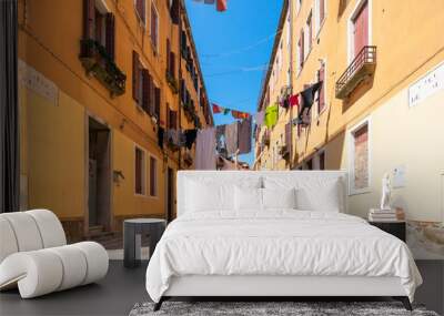 Girl traveler in Venice. A joyful asian woman in red is jumping on Venice street. Colorful laundry is dried on the clotheslines between the houses. Authentic Venetian street in sunshine. Tourism Italy Wall mural