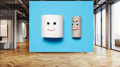 Happy smiling full toilet paper roll next to an angry empty toilet paper roll looking at it with googly eyes and mouth on a blue background Wall mural