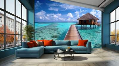 A wooden bungalow sits on stilts over crystal clear water, connected to the shore by a wooden walkway. The turquoise water is shallow and clear, revealing the sandy bottom.  Wall mural