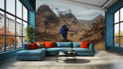 Man photographer with a backpack on the mountain from the back, looking at the mountain valley. The concept of active relaxation, motivation and goal achievement. Glencoe, Scotland, UK. Wall mural