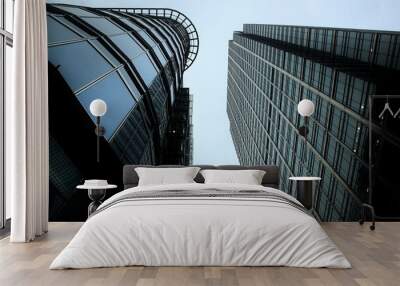 Two towering skyscrapers rise against a cloudy sky, their glass facades reflecting the sombre mood of an overcast day. The modern architecture and steel structures dominate the urban landscape. Wall mural