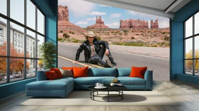 A curly haired blonde man, wearing surprisingly a black leather jacket ,black ripped jeans, black shoes, and a beige linen shirt, majestic beauty of the Monument Valley, Utah and Arizona Wall mural