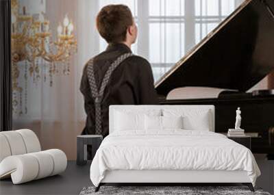 Elegant, handsome young man in black suit and suspenders playing a piano. View from behind. Wall mural