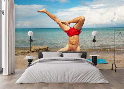 athletic man on beach doing fitness yoga exercise. Acroyoga element for strength and balance. Wall mural