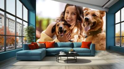 Charming young smiling girl is resting in the park with two golden dogs on a sunny day. The girl hugs her pets. Love and affection between owner and pet. Adopting a pet from a shelter. Close-up. Wall mural