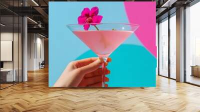 Close-up of a hand holding a pink cocktail garnished with a flower against a colorful background Wall mural