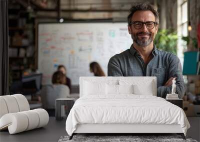 Confident man in casual attire stands with arms crossed in a modern creative workspace with a team collaborating in the background Wall mural