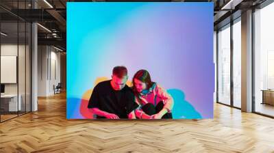 Cool stylish young teen couple with laptop. Colored neon light. Girl and boy bloggers create content for social networks Wall mural