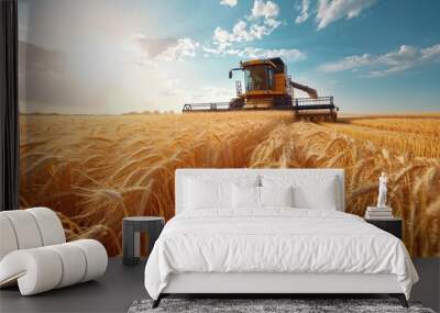 Front view of modern automated combine harvesting wheat ears on a bright summer day. Grain harvester in a vast golden wheat field. Blue cloudy sky with bright sun in the background. Wall mural