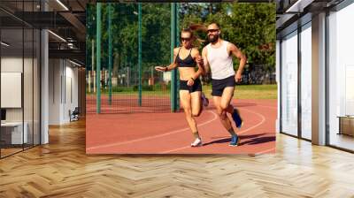 Handsome young athletes looking at the camera and smiling while training at the city stadium, diversity men and women are jogging. Wall mural