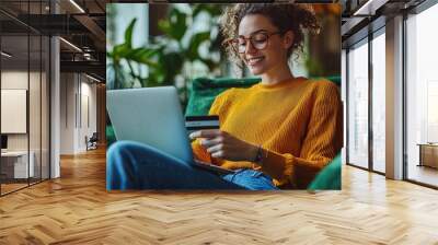 Happy woman shopping online at home with a laptop and credit card, enjoying a relaxing moment in a cozy living room Wall mural