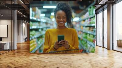 Happy woman using her mobile phone while shopping in a grocery store aisle with fresh produce and colorful products Wall mural