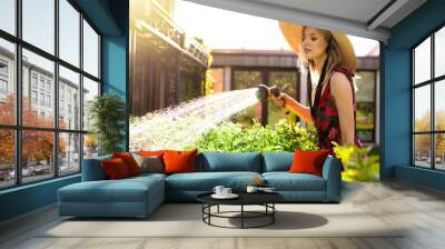 Pretty young girl in a hat watering plants with a garden hose in the garden in summer, photography for blog or ad Wall mural