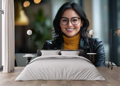 Smiling woman in her late thirties with glasses and a leather jacket working on a laptop at a modern cafe Wall mural