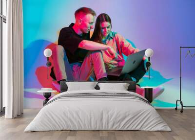 Stylish young couple with laptop working, watching series or shopping online. Colorful neon light Wall mural