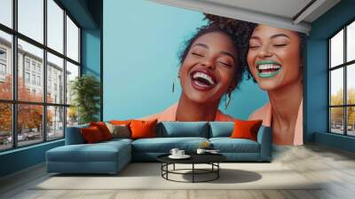 Two beautiful women in peach blazer suits sharing joyful laughter against a vibrant blue background Wall mural