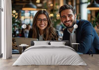 Two happy professionals, a man and a woman, smiling confidently in an office setting with a laptop, exuding teamwork and collaboration Wall mural