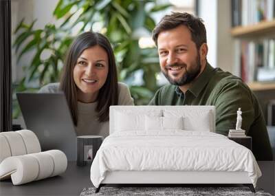 Two young professionals smiling confidently while working together on a project in a modern office with greenery Wall mural