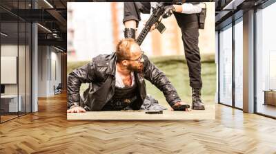 Woman soldier, spy agent killer or police woman with a gun in her hand holding at gunpoint a man lying on the ground Wall mural