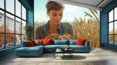 Young woman in casual attire picks ripe golden wheat on a sunny day in a vast field Wall mural