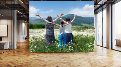 Two happy women with a teenage girl standing hands up enjoying beautiful view of the blossoming meadow near mountains in Armenia in summer day. View from behind Wall mural