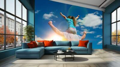 Father and daughter are playing outdoors, against the sky and sun. A happy child is sitting on his shoulders. Wall mural