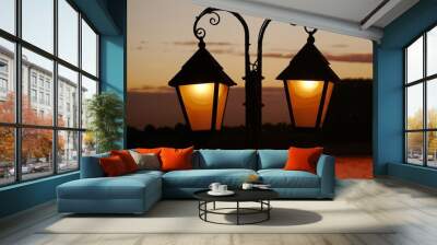 Wrought-iron lantern illuminated, as a silhouette in front of the sky illuminated by the sunset in the blurred background. Enough space on the windows of the lantern to insert your own text. Wall mural