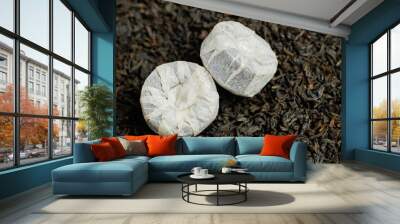 Two pressed tea tablets wrapped in wrapping paper on background of black tea. Wall mural