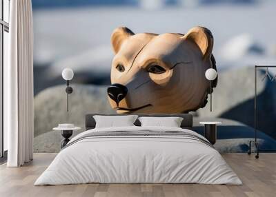 A wooden carving of a bear's head sits on a rock with a blurry background of a frozen landscape. Wall mural