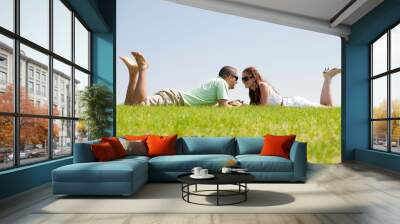 Playful young couple laying on a grass lawn Wall mural