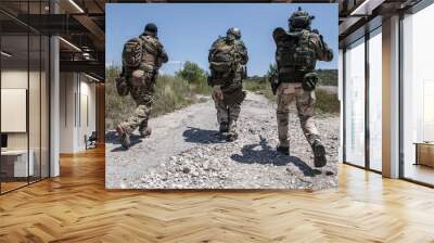 Army soldiers team in combat uniform, load carriers and helmets running on countryside road, aiming guns and sneaking in bush. Special forces infantrymen group moving with cautious at abandoned area Wall mural