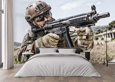 Close up portrait of army special forces soldier, commando rifleman, SEALs fighter with dirty face, wearing shemagh scarf, combat helmet and ballistic glasses, aiming and shooting with submachine gun Wall mural