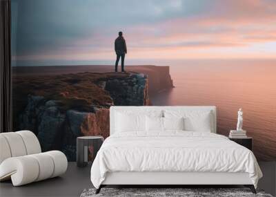 Man standing on the edge of a cliff and looking at the sunset,Silhouette of a man standing on the edge of a cliff in the fog. Wall mural