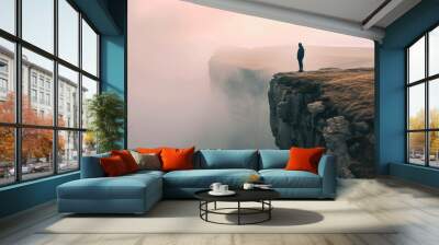 Man standing on the edge of a cliff and looking at the sunset,Silhouette of a man standing on the edge of a cliff in the fog. Wall mural