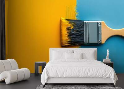 A paintbrush with yellow paint is shown in the middle of a blue and yellow surface. The brush is angled towards the right side of the image. Wall mural