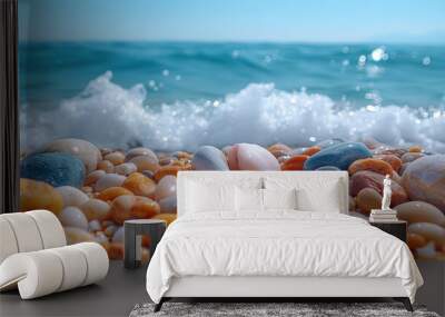 Close-up of smooth, colorful pebbles on a beach, with a gentle wave breaking in the background. Wall mural