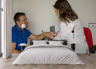 Doctor in her office with a patient while measuring his blood saturation with an oximeter Wall mural