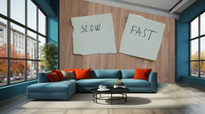 Two sticky notes on the table, one says SLOW, and the other reads Fast. The background is wooden, with Wall mural