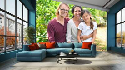 Portrait of smiling parents with daughter sitting on bench in garden Wall mural