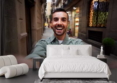 Happy selfie of a young caucasian man in an old town of Barcelona. Male tourist taking a self portrait using smartphone to post it on social media, Wall mural