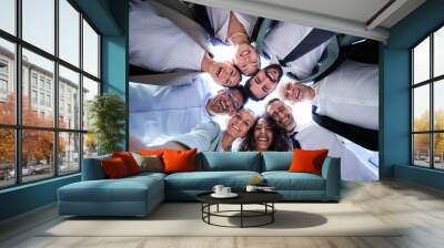 Multiethnic group of work colleagues embraced in circle, face down taking a selfie smiling and looking at the camera. POV business people doing team building.  Wall mural