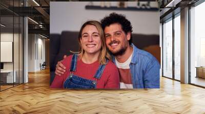 Sweet portrait of a young caucasian couple looking at camera smiling at home. Wall mural