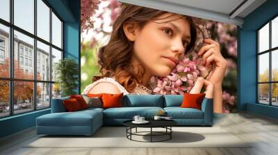 young woman posing with blooming pink sakura flowers tree branch in spring orchard Wall mural