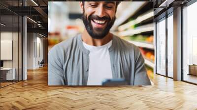 A young man laugh while looks the cell phone in the supermarket Wall mural